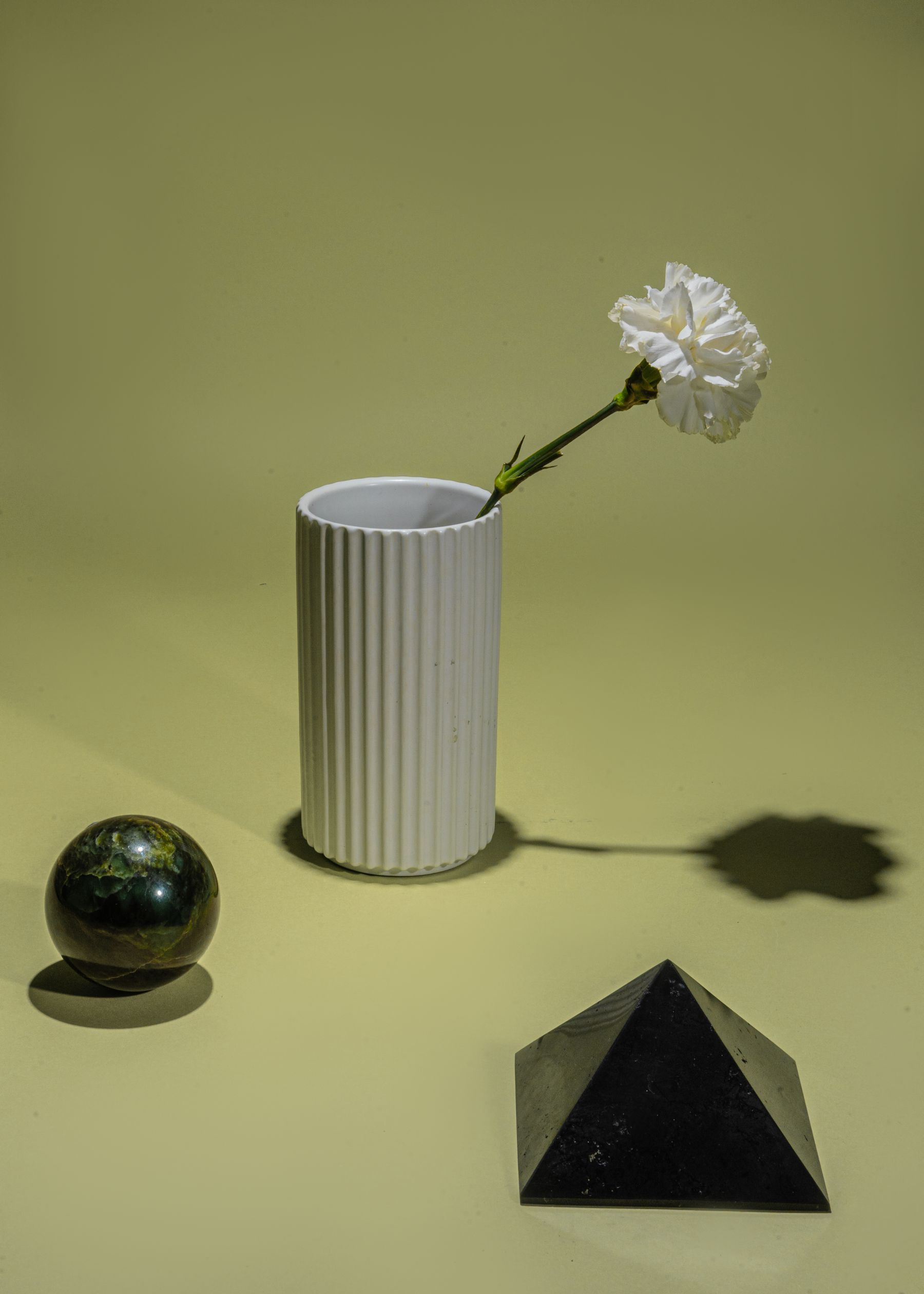 A ribbed vase and a dark sphere on green