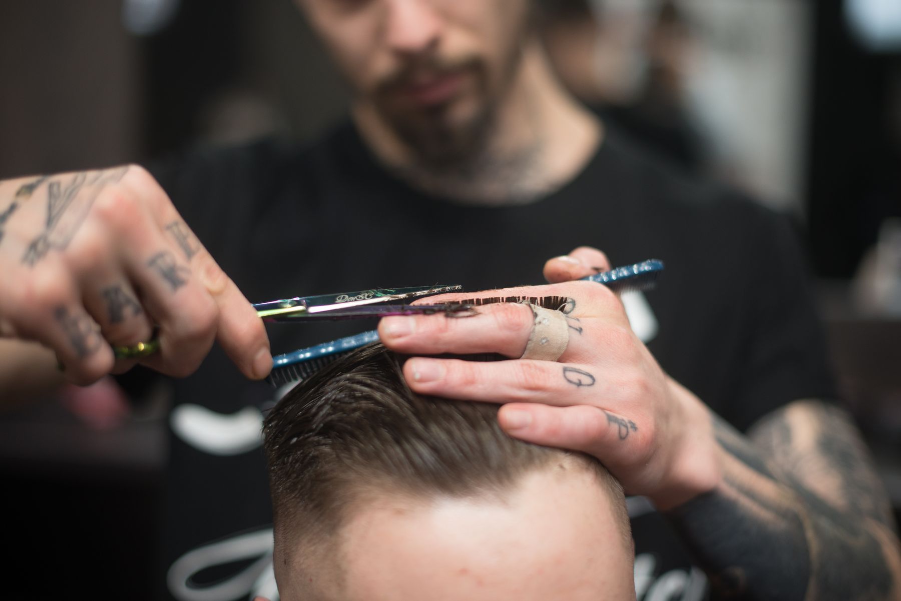 A tattooed barber cutting hair with scissors