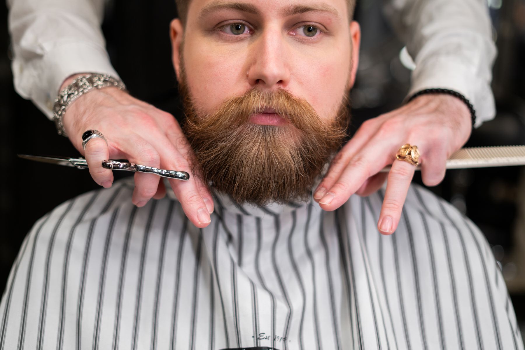 A barber trimming a red beard