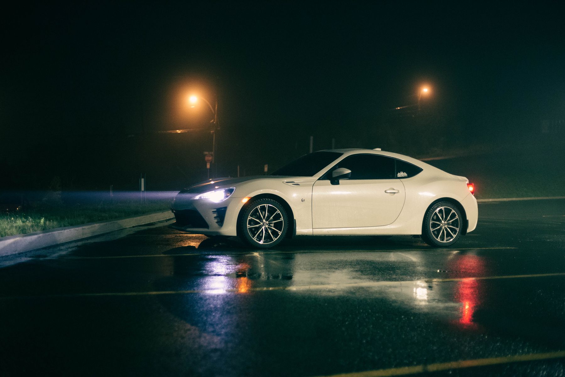 A white sports coupe on a wet car park at night