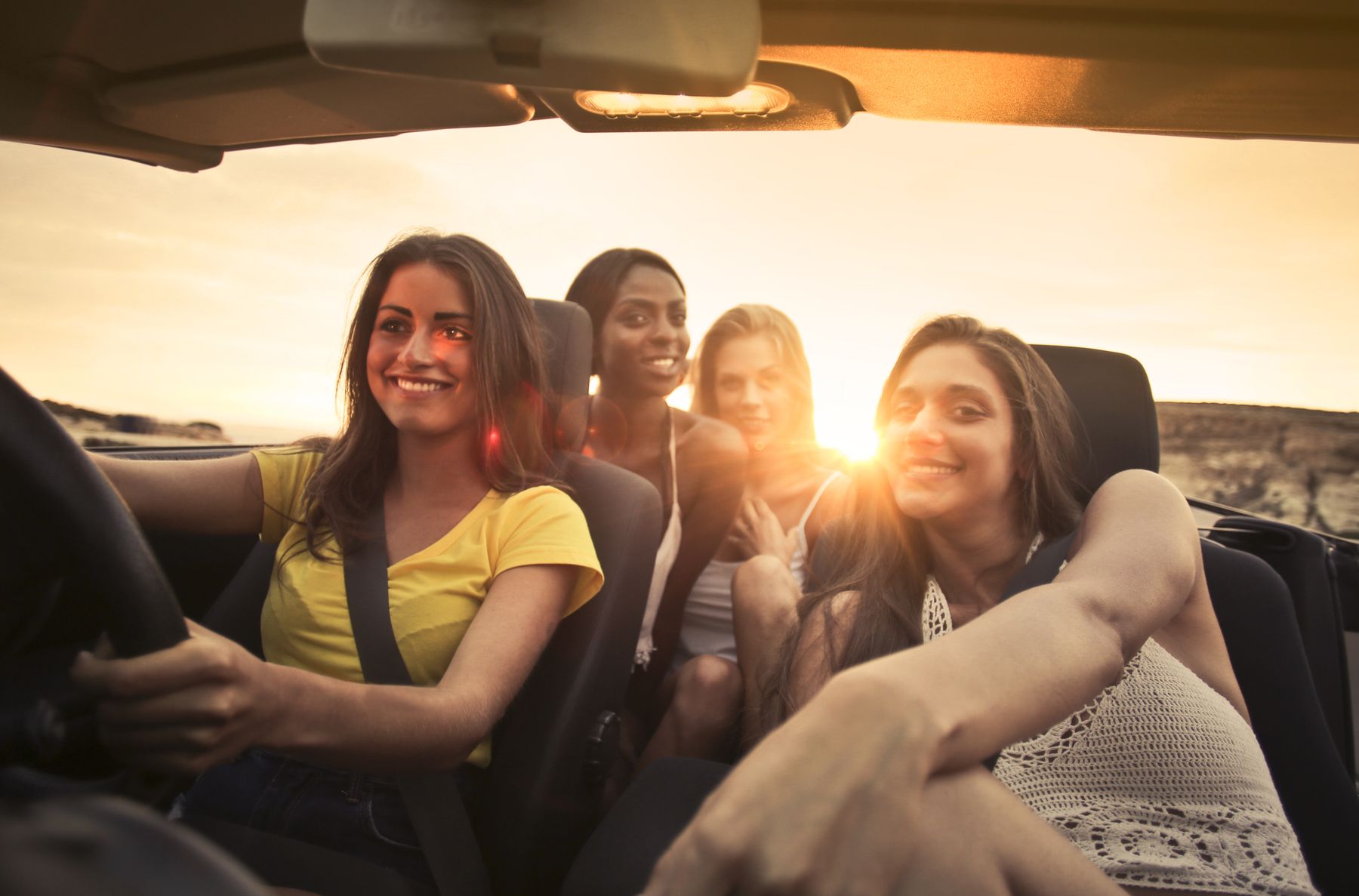 Friends laughing in a convertible at sunset
