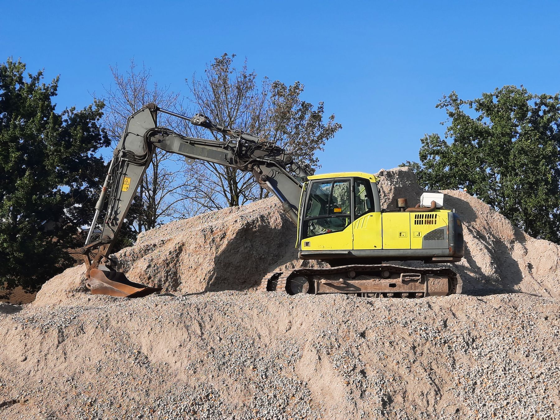 A yellow-green excavator moving earth on a construction site