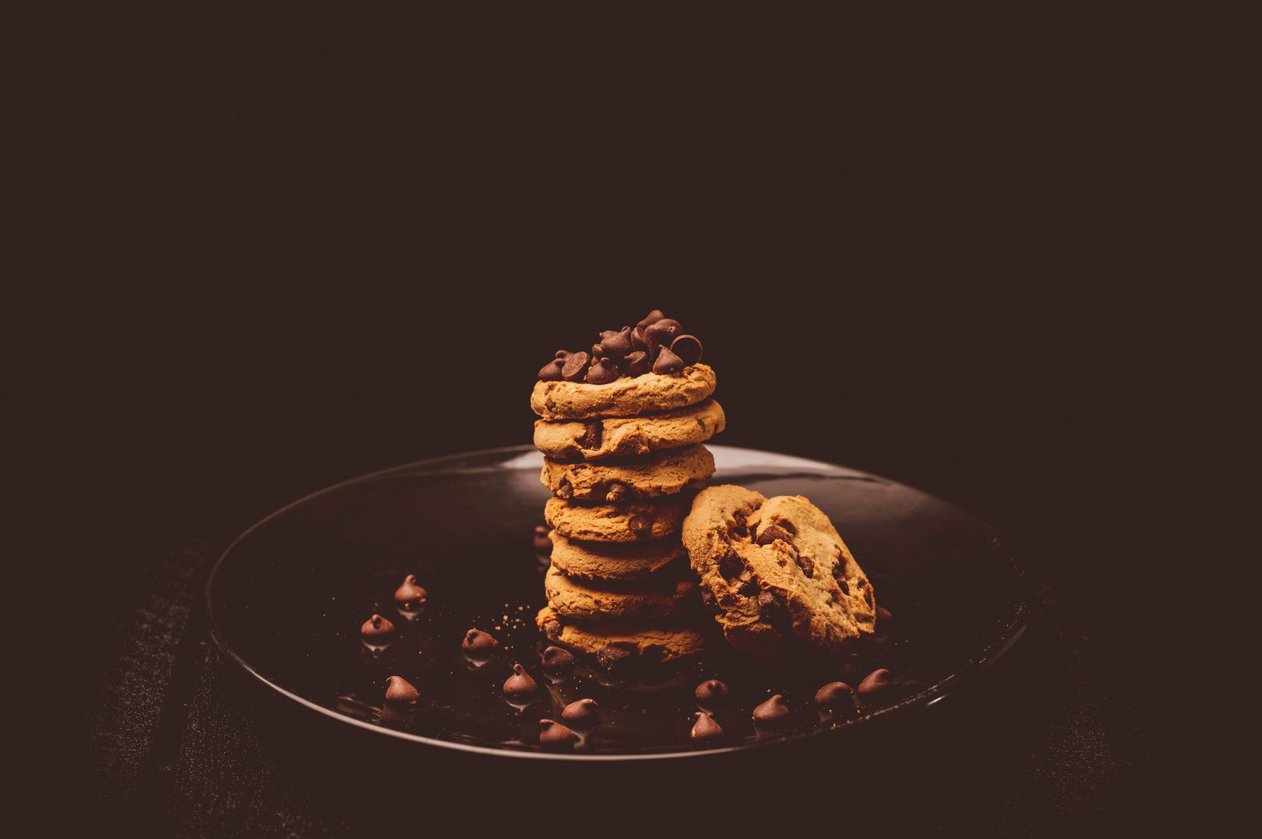 A stack of chocolate chip cookies on a dark plate