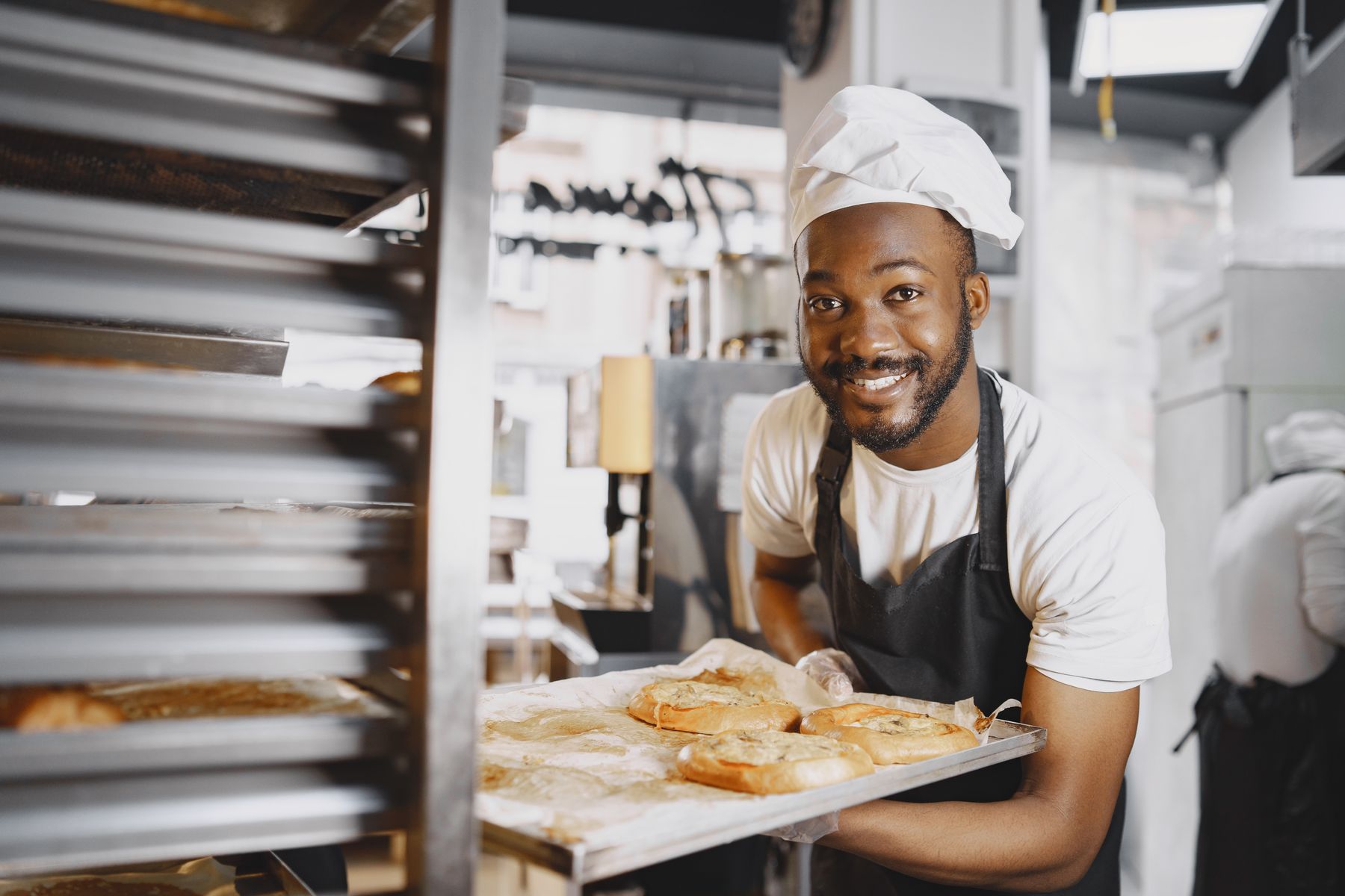 A smiling baker holding a tray of bread