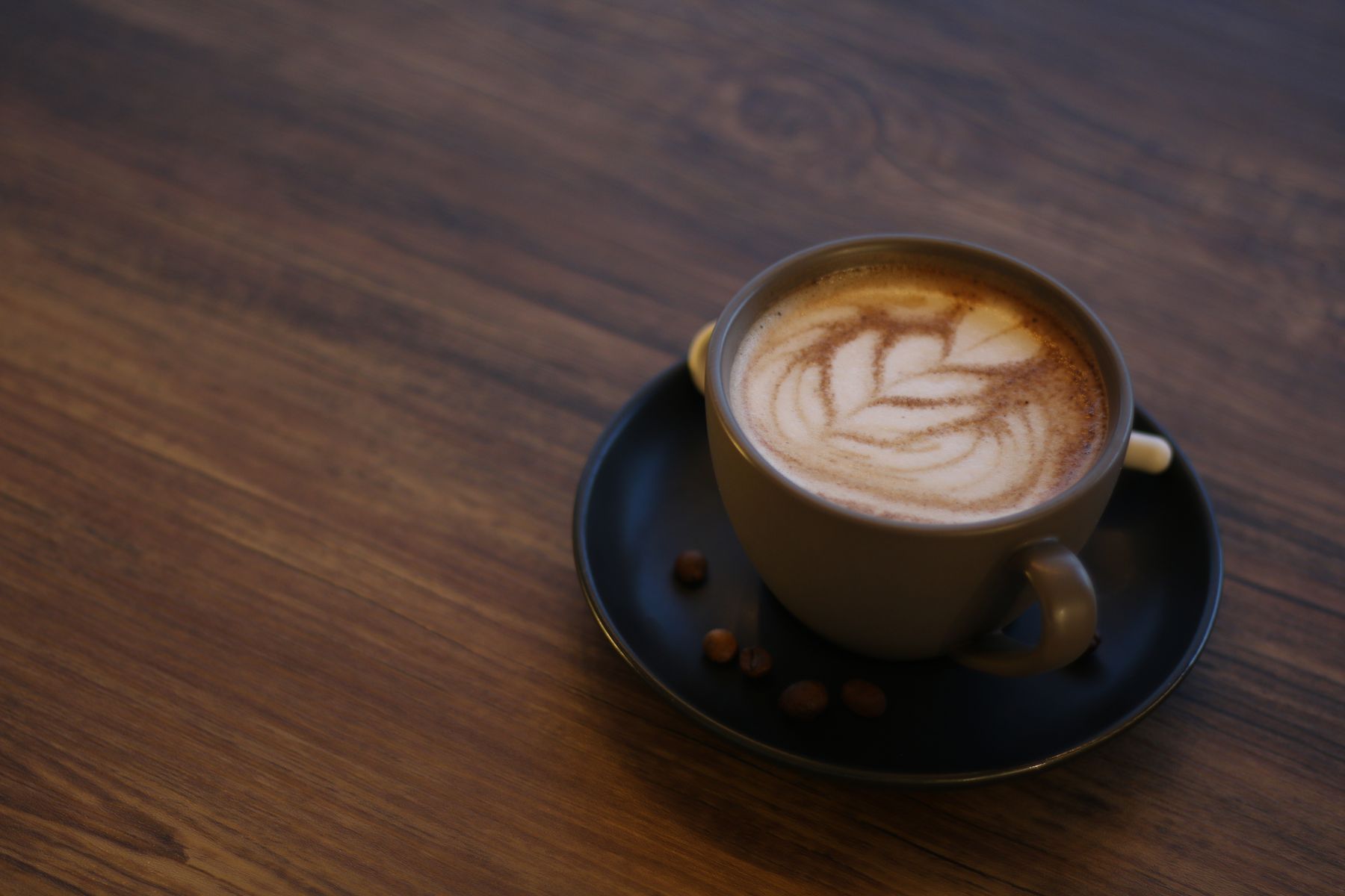 A latte with leaf art on a dark wooden table