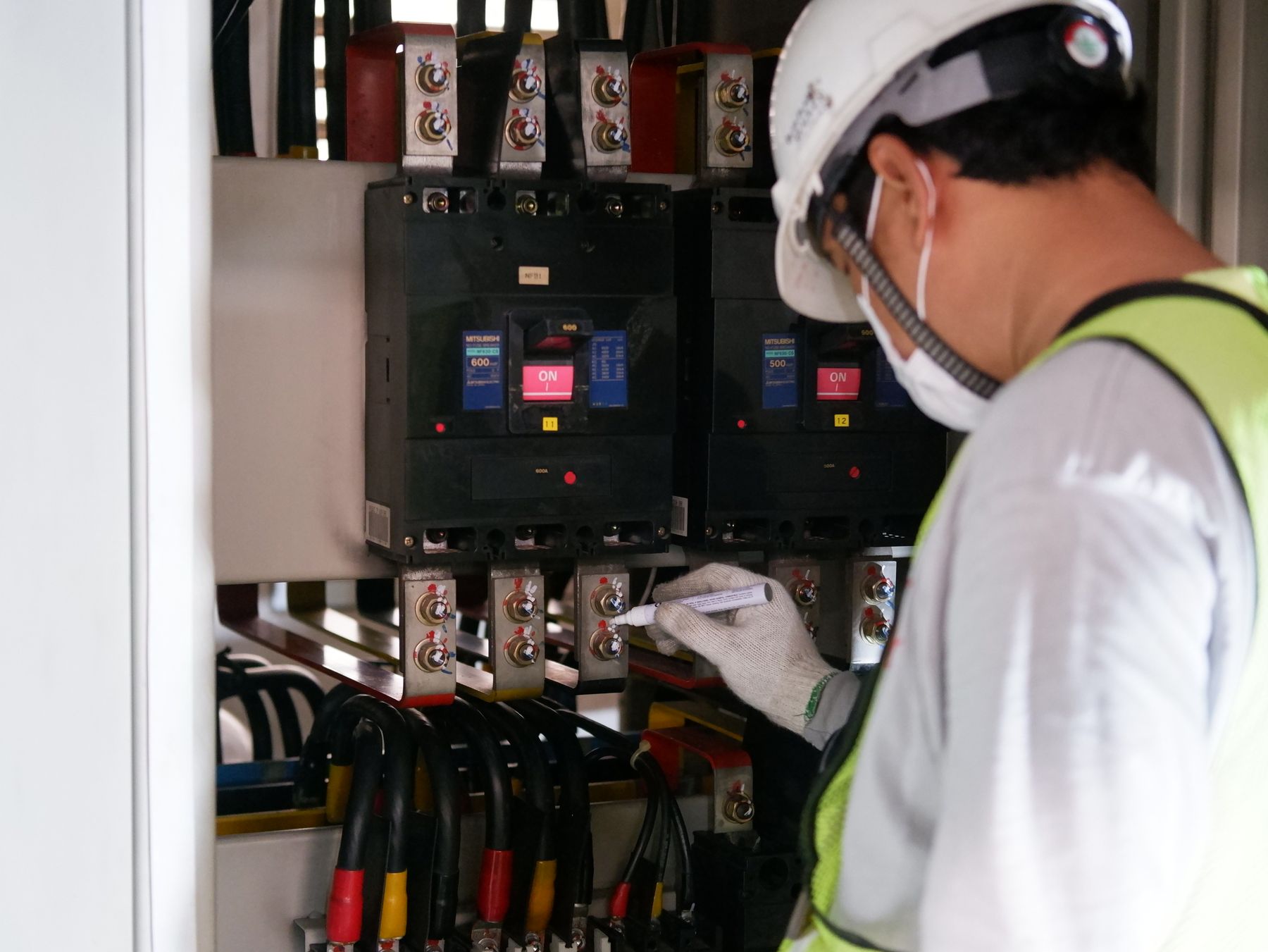 An electrician in a hard hat working at a distribution board