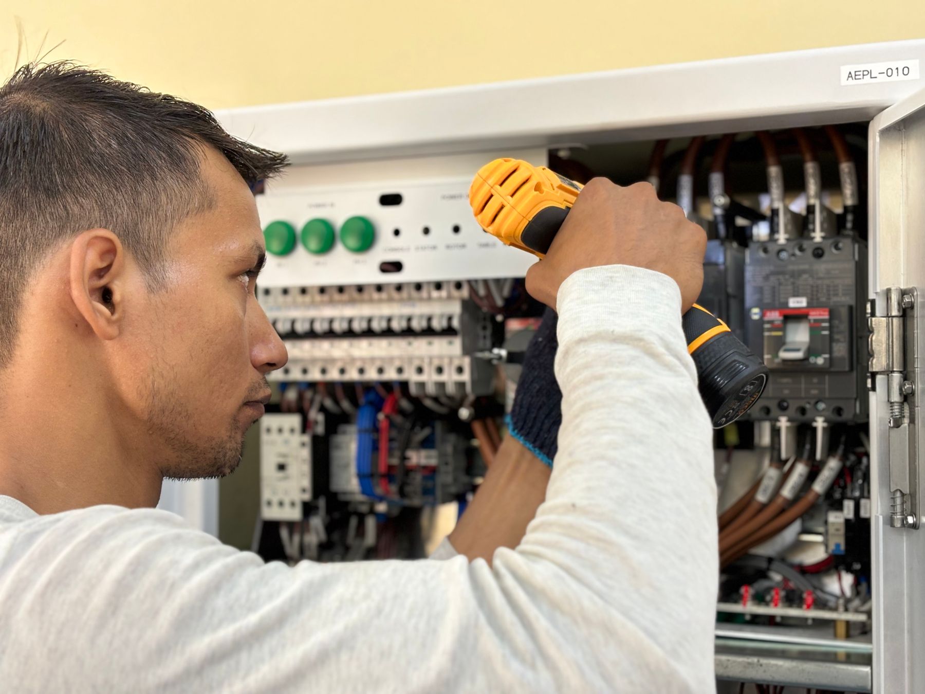 An electrician using a drill inside a control panel
