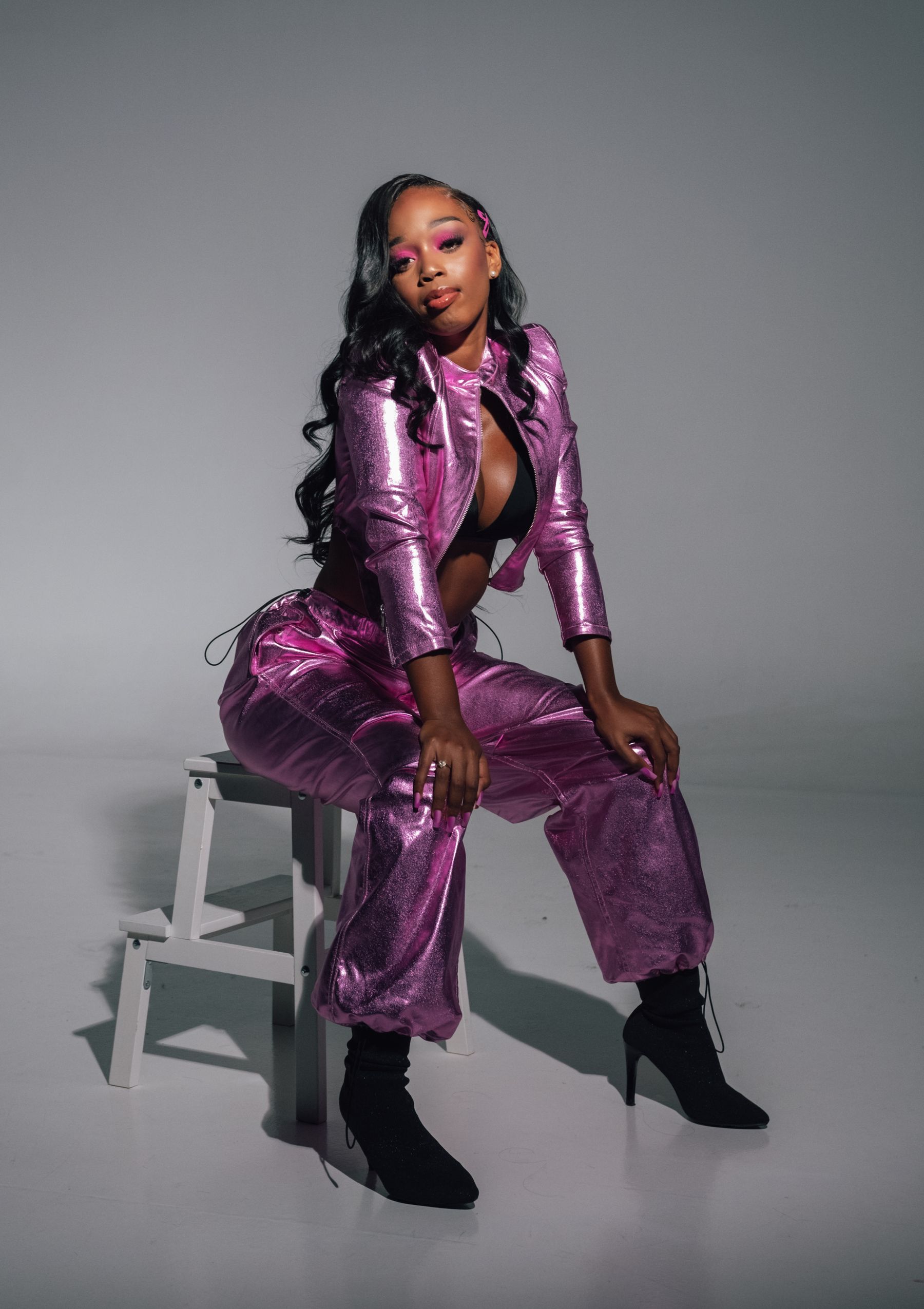 A model in a metallic purple tailored suit seated in a studio